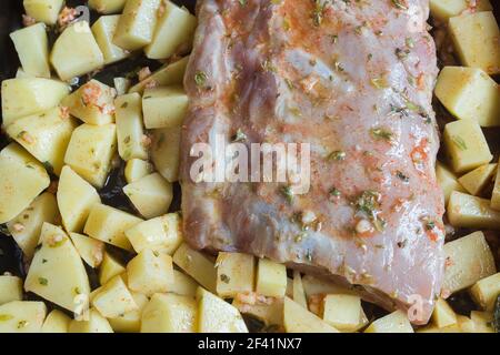 Vue en hauteur des côtes de porc fraîches et des pommes de terre coupées en carrés baignés dans une sauce à l'ail, à l'huile, au vinaigre et à l'origan. Aliments frais et viandes crues. Banque D'Images