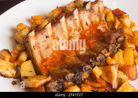 Une délicieuse assiette de côtes levées avec sauce épicée et pommes de terre cuites au four. Faire cuire la viande. Banque D'Images