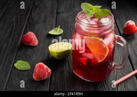 Limonade froide avec fraises et lime sur fond de bois noir. Gros plan. Banque D'Images