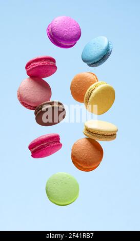 Macarons doux colorés ou macarons, biscuits aromatisés flottant dans l'air sur fond bleu. Banque D'Images