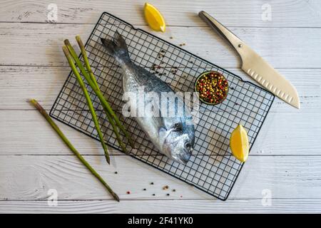 Un poisson frais sur une grille entourée de citron, d'asperges sauvages, d'un couteau et de grains de poivre Banque D'Images