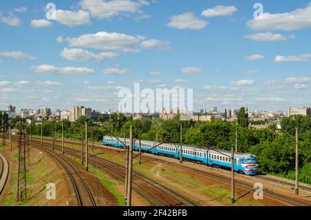 Un vieux train électrique se déplace sur des rails en été, sur fond de paysage urbain et de gratte-ciel à la lumière du soleil. Banque D'Images