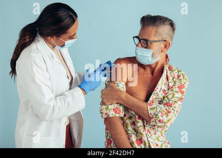 Homme mature recevant la deuxième dose de vaccin du coronavirus pour une immunité complète. Médecin donnant le vaccin à un homme portant un masque facial pendant une pandémie. Banque D'Images