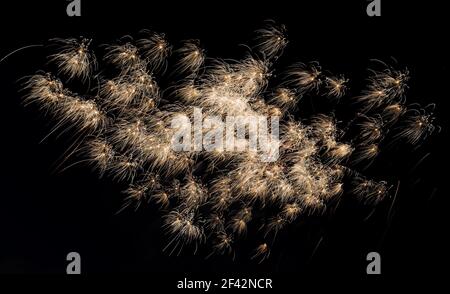 Gros plan sur les feux d'artifice orange blancs la nuit. Les feux d'artifice sont isolés, rien d'autre n'est visible. Le vent souffle les banderoles. Il y a beaucoup de détails. Banque D'Images