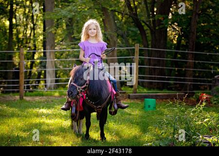 Belle fille blonde en chemise pourpre à cheval un petit poney noir. Banque D'Images