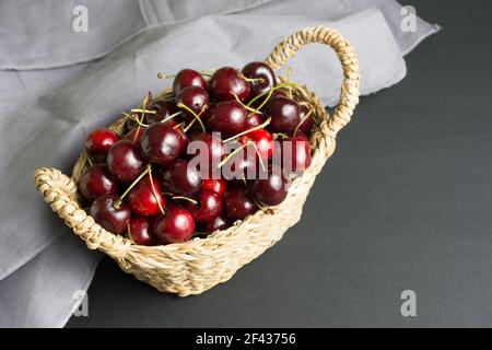 panier en osier rempli de cerises en tissu gris et noir arrière-plan Banque D'Images