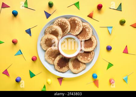 Assiette de petites crêpes rondes avec drapeaux de fête colorés sur fond en papier à trois couches de couleur. Vue de dessus, couleurs vives et vives, orange Banque D'Images