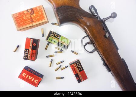 Concept de chasse avec un fusil à action boulon et des boîtes vintage de balles de calibre .22 et des balles libres dispersées sur un fond blanc. Banque D'Images