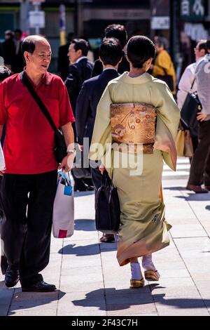 Vue arrière sur toute la longueur de la femelle japonaise marchant à travers Ginza portant un kimono sous le soleil de l'après-midi, Tokyo, Japon Banque D'Images