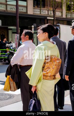 Vue arrière profil de la jolie japonaise femelle marchant à travers Ginza portant un kimono vert lime dans le soleil de l'après-midi, Tokyo, Japon Banque D'Images