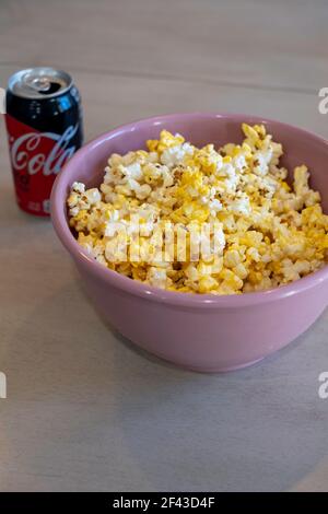 Pop-corn, ou maïs soufflé, dans un bol rose sur une table avec une CAN de Coca-Cola Zero, une boisson gazeuse. Banque D'Images