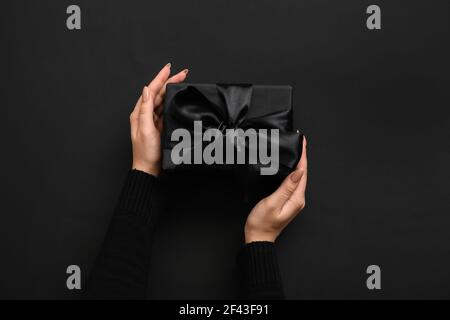 Mains de femmes avec boîte cadeau sur fond sombre Banque D'Images