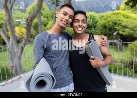 Portrait de divers couples homosexuels hommes tenant des tapis de yoga et sourire sur le balcon Banque D'Images