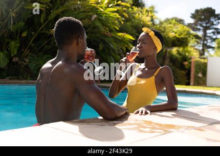 Couple afro-américain en eau potable au bord de la piscine terrasse de jardin ensoleillée Banque D'Images