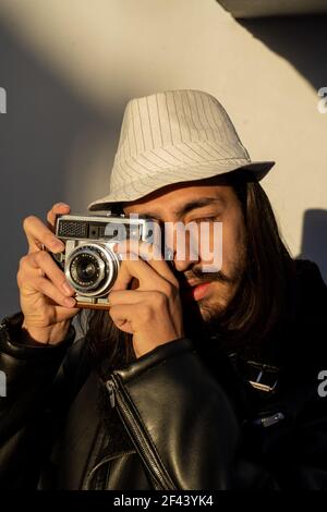 Gros plan d'un homme élégant avec une tenue rétro prenant une photo avec un appareil photo vintage. Photographe latin concentré travaillant à l'extérieur. Avec le soleil. natur Banque D'Images