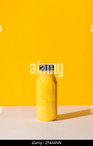 Smoothies de couleur jaune dans une bouteille sur fond jaune avec des ombres dures. Le concept de nutrition sportive. Banque D'Images