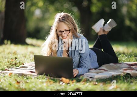 Bonne blonde étudiant sur ordinateur portable au parc Banque D'Images