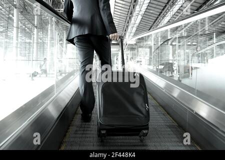 Homme d'affaires tenant le sac du chariot à monter sur l'escalier roulant à l'aéroport Banque D'Images