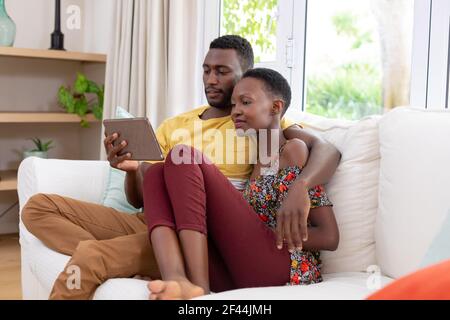 Couple afro-américain assis sur un canapé avec une tablette et souriant Banque D'Images