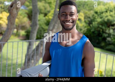 Portrait d'un homme afro-américain tenant un tapis de yoga souriant terrasse de jardin ensoleillée Banque D'Images