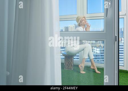 Vue par la fenêtre d'une femme assise le balcon de son nouvel appartement Banque D'Images