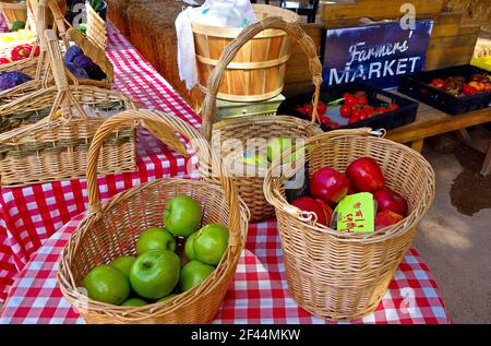 Un gros plan de paniers remplis de gros rouge doux et des pommes vertes avec un panier de tomates dans le arrière-plan Banque D'Images