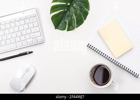 Espace de travail avec clavier d'ordinateur, fournitures de bureau, feuille verte et tasse à café sur fond blanc. Banque D'Images