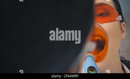 vue rognée d'une femme dans des lunettes près d'un dentiste avec lampe à ultraviolet, avant-plan flou Banque D'Images