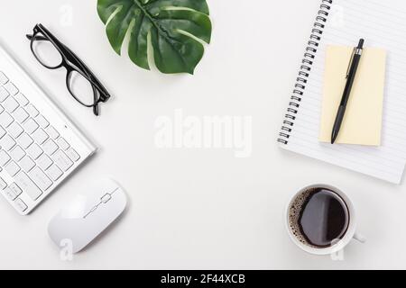 Espace de travail avec clavier d'ordinateur, fournitures de bureau, feuille verte et tasse à café sur fond blanc. Banque D'Images