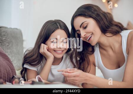 Visage de maman satisfait avec un crayon cosmétique et une fille Banque D'Images