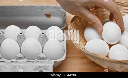 vue courte de l'homme prenant l'oeuf du panier en osier près plateau à œufs sur une table en bois Banque D'Images