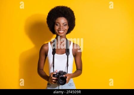 Portrait de charmante jeune fille à cheveux ondulés et fins tenant entre les mains caméra digicam isolée sur fond jaune vif Banque D'Images