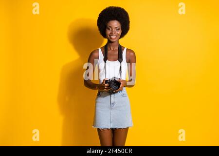 Portrait d'une jeune fille mince et gaie aux cheveux ondulés tenant entre les mains photo de prise de vue digicam isolée sur fond jaune vif Banque D'Images