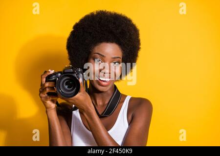 Portrait en gros plan d'une jolie fille de brunette aux cheveux ondulés qui tient dans mains utilisant la prise de vue digicam isolé sur fond jaune vif Banque D'Images