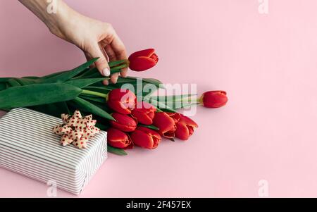 Sur fond rose, un bouquet de fleurs et une boîte cadeau. La main femelle tient une fleur de tulipe Banque D'Images