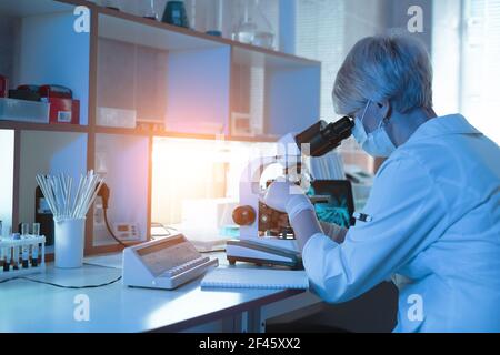 Femme médecin médecin ou chercheuse à travers un microscope dans un laboratoire.science expériences, verrerie de laboratoire contenant des produits chimiques Banque D'Images