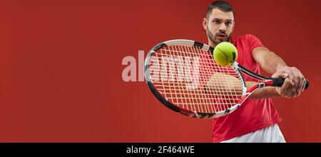 En-tête de site Web de l'athlète sérieusement fort homme dans le maillot rouge jouer au tennis isolé sur fond rouge Banque D'Images