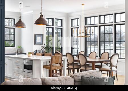 Une cuisine et une salle à manger luxueuses avec des lumières suspendues au-dessus de l'île et un lustre au-dessus de la grande table. Banque D'Images