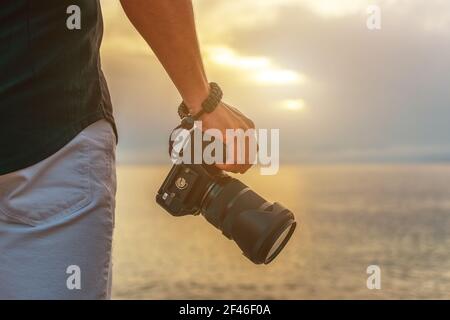 L'homme tient un appareil photo dans la main au coucher du soleil. Banque D'Images