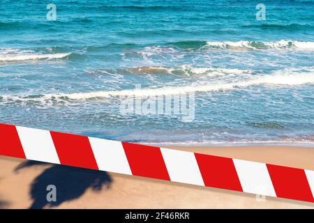 Ruban barrière - quarantaine, concept d'isolement, interdiction d'entrée. Ne pas croiser. Ombre des palmiers sur l'eau de mer sur la plage. Banque D'Images