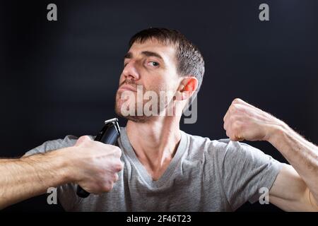 Homme au visage amusant tenant le rasoir sans fil avant de se raser, sur fond noir. Banque D'Images