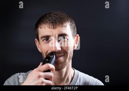 Portret d'homme utilisant la tondeuse nez gros plan, sur fond noir. Banque D'Images