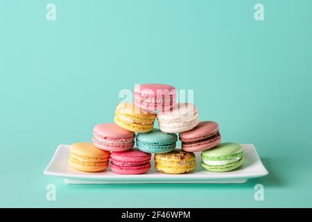 Pyramide de macarons colorés sur une plaque rectangulaire blanche sur fond turquoise pastel. Maquette de carte de vœux avec des macarons multicolores doux. Banque D'Images