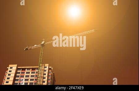 Vue de dessous d'un bâtiment de plusieurs étages et d'une grue de construction sur fond de ciel orange. Coucher de soleil Banque D'Images