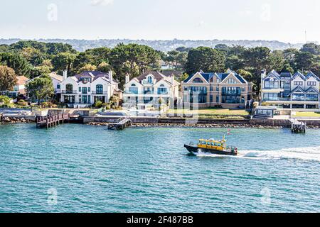 Le bateau-pilote du harbormaster passe devant des maisons de luxe sur la péninsule de Sandbanks, dans le port de Poole, au Royaume-Uni Dorset Banque D'Images