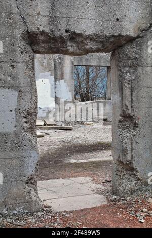 Vue verticale à travers le couloir d'un ancien abandonné structure en béton à travers la fenêtre manquante éloignée vers le ciel bleu et arbres dehors Banque D'Images