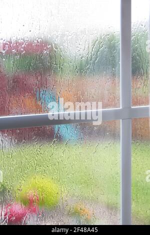 Vue verticale de l'aire de jeux de l'arrière-cour par jour de pluie à travers la fenêtre sectionnée et protégée légèrement floue par la pluie tombant. Pâte fonctionnelle Banque D'Images