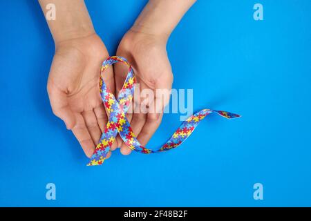 Journée mondiale de sensibilisation à l'autisme. Mains autistes de garçon tenant le ruban de motif de puzzle sur fond bleu Banque D'Images