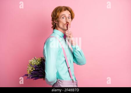 Photo portrait de l'homme aux cheveux rouges en gardant le secret donnant des fleurs le jour faisant la surprise isolée sur fond rose pastel Banque D'Images