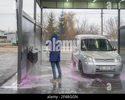 Un homme couvre un auto avec de l'eau à un libre-service lavage de voiture Banque D'Images